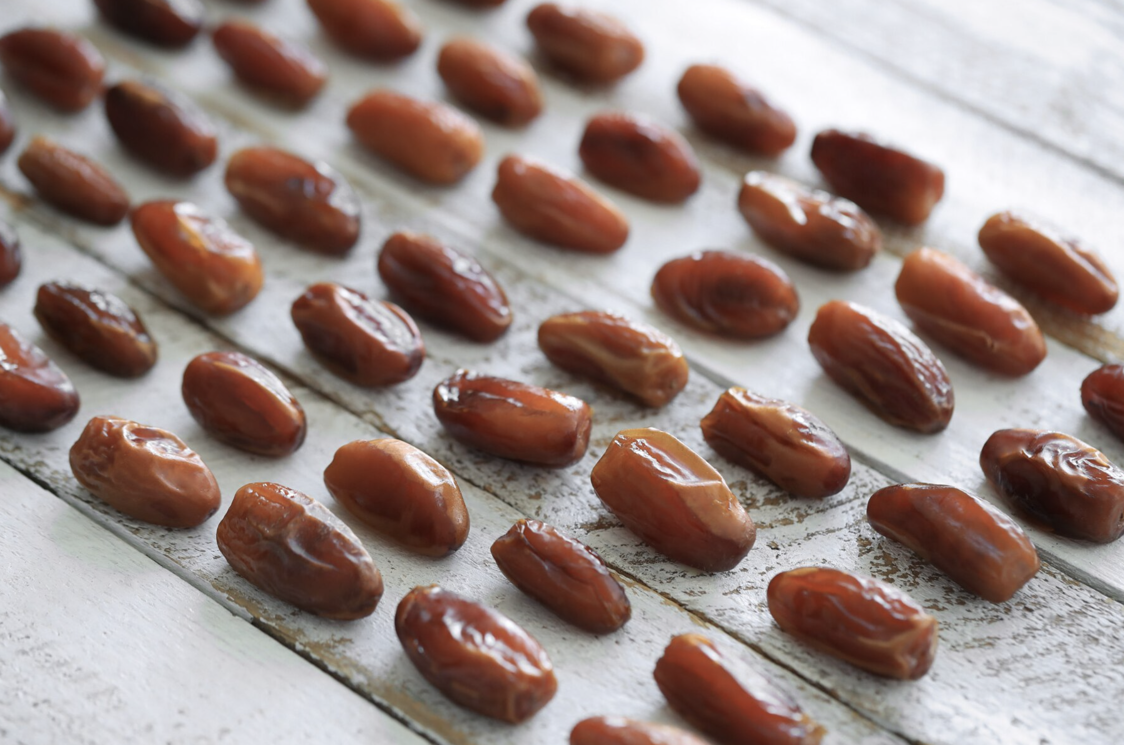 Rows of fresh, glossy Medjool dates neatly arranged on a white wooden surface, perfect for creating Date Recipes for Breakfast.