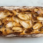 Close-up of a freshly baked loaf of sourdough bread with roasted garlic cloves peeking through the cracks in the crust.